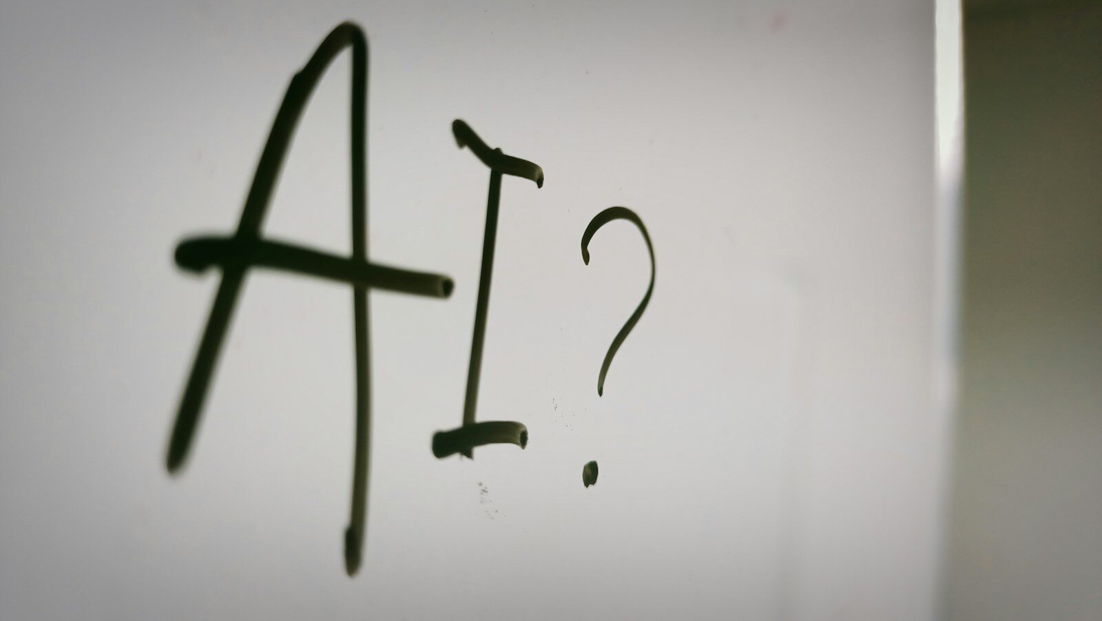 The letters AI and a question mark written in black marker on a whiteboard